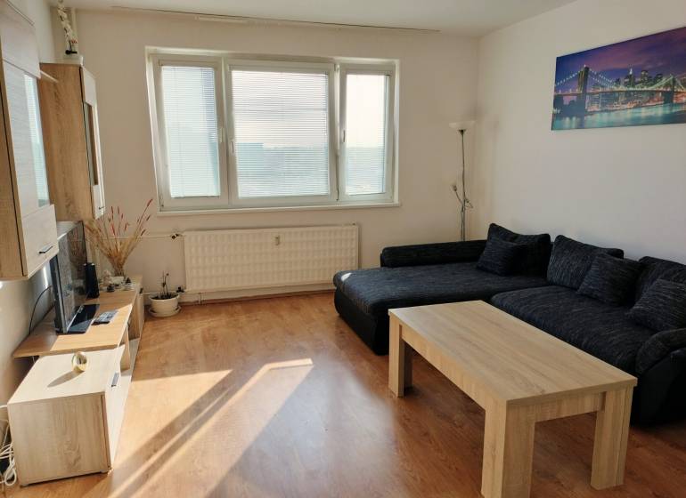 Nappali kanapéval, dohányzóasztallal és fa dekorációjú padlóval egy háromszobás lakásban.