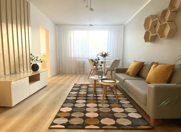 Nappali egy kétszobás lakásban, fa mintázatú padlóval és mintás szőnyeggel.