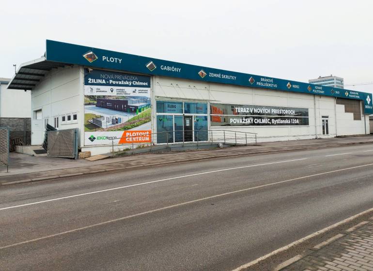 Üzlethelyiségek a Kő utcában, Zsolnán, reklámfeliratokkal és üres parkolóval.