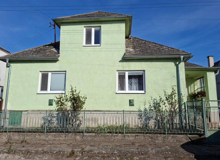 Családi ház Kisleváron világoszöld homlokzattal és meredek tetővel.
