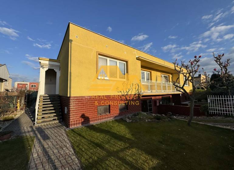 Sárga családi ház Érsekújváron, rendezett kerttel és járdával az utcán.