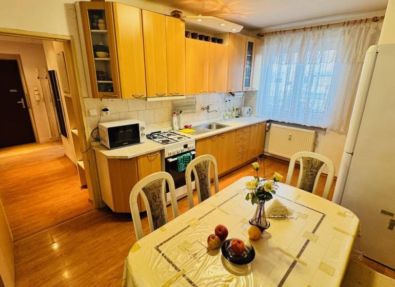 Konyha egy háromszobás lakásban, fa dekor padlóval és étkezőasztallal.