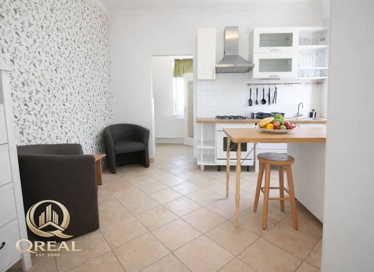 Konyha bárpulttal, gyümölcsökkel és székekkel egy egyszobás lakásban.