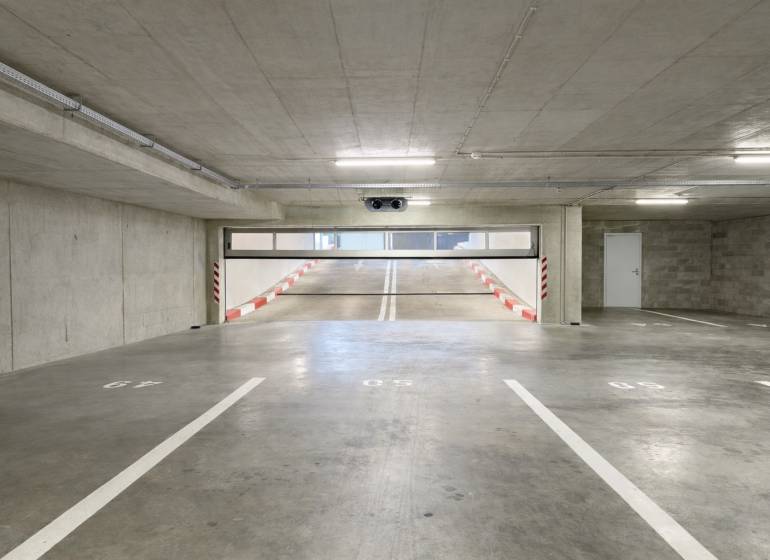 Parkolóhelyek garázsokban rámpával és fehér jelöléssel.