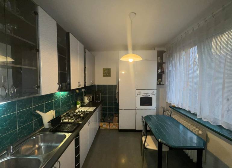 Konyha egy kétszobás lakásban sötétzöld csempékkel és fa dekoros padlóval.