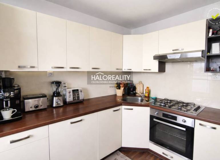 Konyha egy 4 szobás lakásban fehér szekrényekkel és fa hatású padlóval.