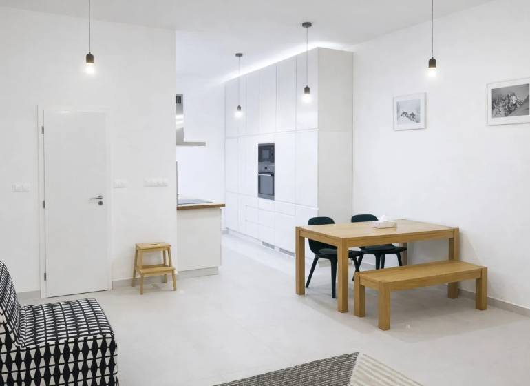 Egy 2 szobás lakás belső tere fehér falakkal, fa asztallal és fekete kanapéval.