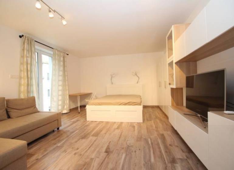 Nappali zóna egyszobás lakásban ággyal és fa dekor padlóval.