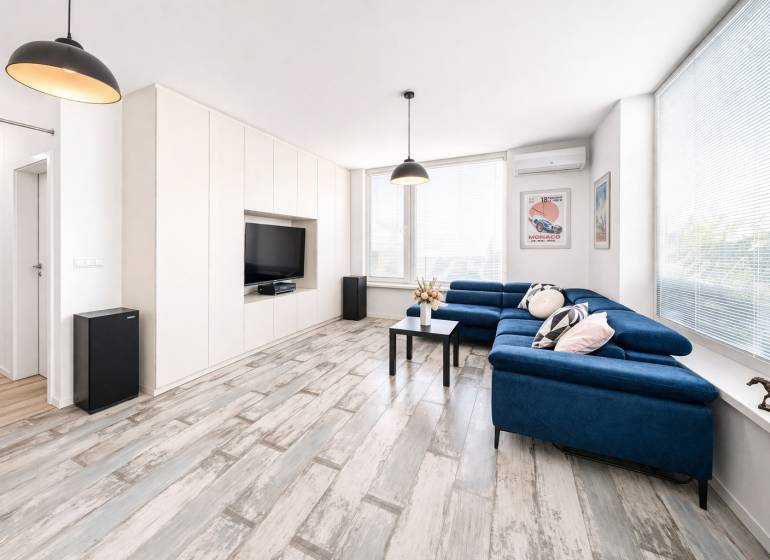 Nappali egy kétszobás lakásban kék kanapéval és fa dekorációjú padlóval.