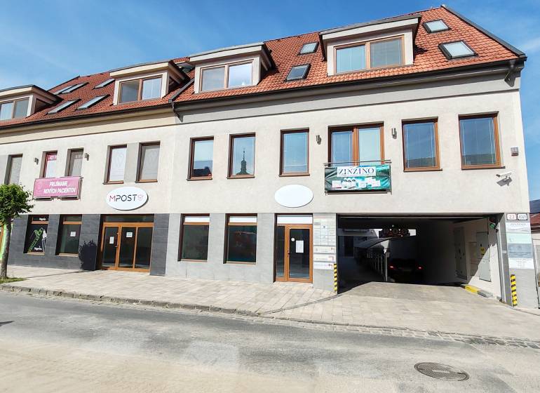 Üzlethelyiségek Nagyszombatban fehér homlokzattal, piros tetővel és reklámfeliratokkal.