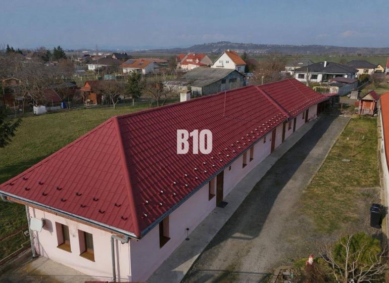 Egy családi ház Léva városában hosszú piros tetővel, kertek által körülvéve.