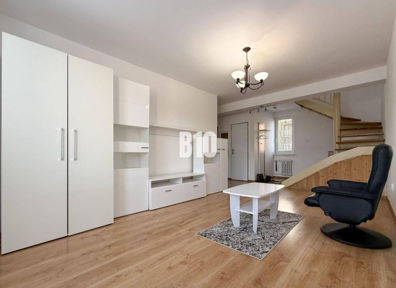 Nappali a nyaraló apartmanban fehér bútorokkal és fa mintás padlóval.