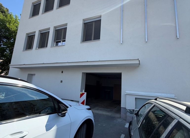Épület garázsokkal a Prievidza, Hosszú utca 3 alatt, parkoló autók az épület előtt.