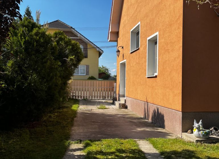 Családi ház Csallóközben narancssárga homlokzattal, gyepesített udvarral és szilárd burkolatú bejárati úttal.
