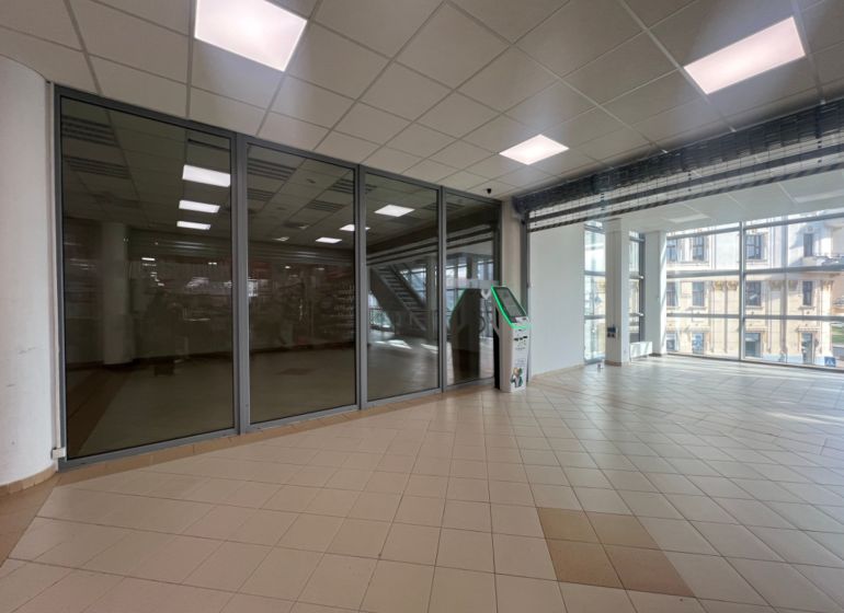 Üvegfalú üzlethelyiségek csempével és bankautomatával, belső tér nagy ablakokkal.