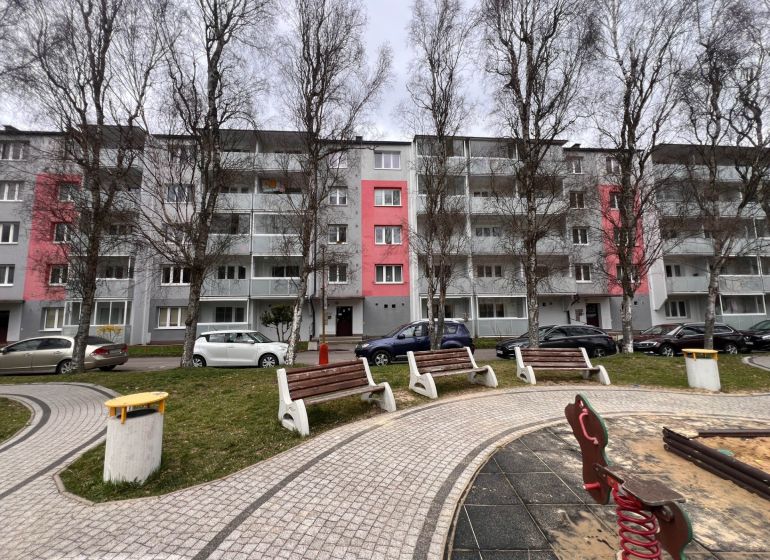 Egy lakóház Rózsahegyen, fákkal és parkolóhelyekkel a kétszobás lakások előtt.