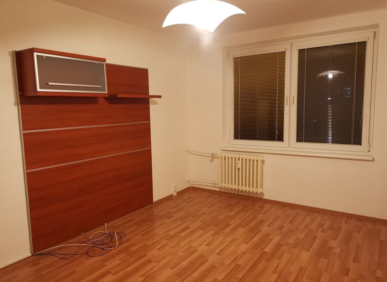 Szoba fa dekoros padlóval, fehér falakkal és fali szekrénnyel egy háromszobás lakásban.