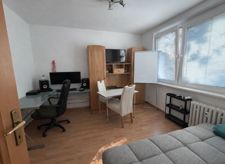 3 szobás lakás belső tere fa dekor padlóval, íróasztallal és kanapéval.