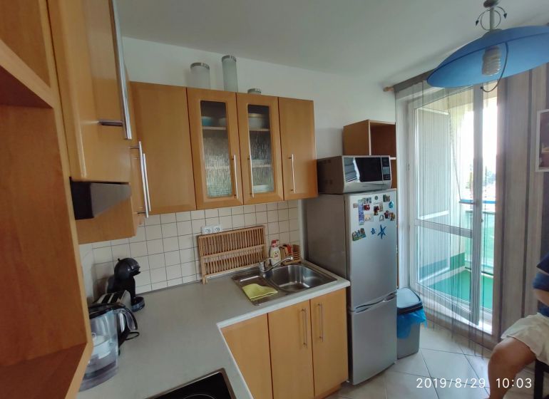 Konyha fa szekrényekkel, mikrohullámú sütővel és hűtőszekrénnyel egy kétszobás lakásban.