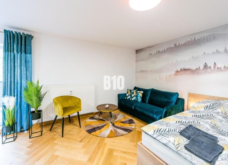 Stílusos nyaraló apartman fa hatású padlóval, kanapéval és növényekkel.