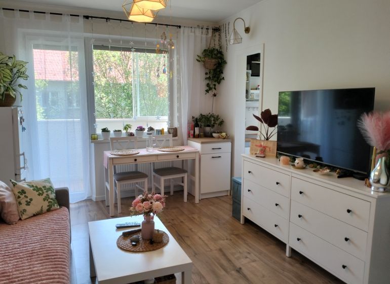 Nappali egy egyszobás lakásban, fa dekor padlóval és fehér bútorokkal.