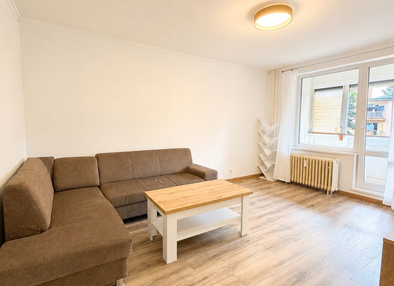 Nappali egy háromszobás lakásban kanapéval, dohányzóasztallal és fa dekorációjú padlóval.