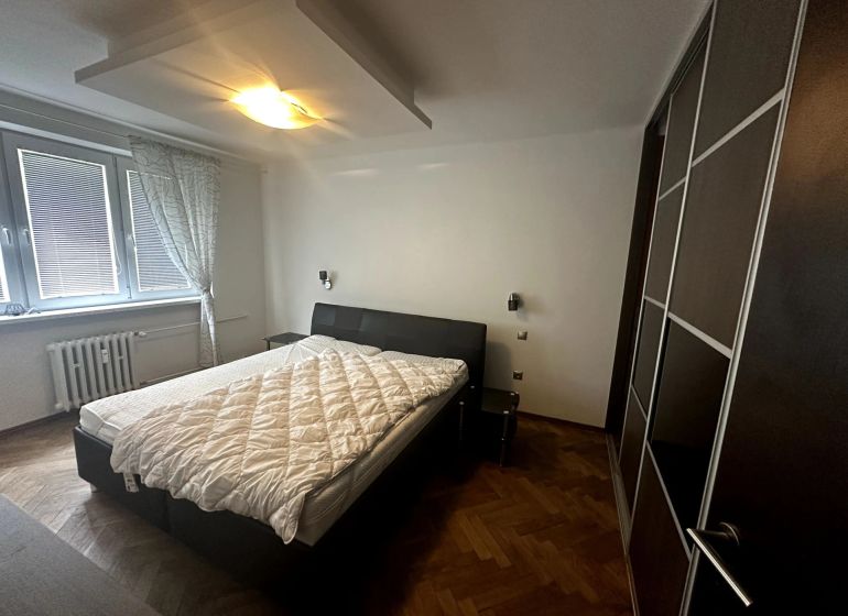 Hálószoba egy kétszobás lakásban, ággyal, gardróbszekrénnyel és fa dekoros padlóval.
