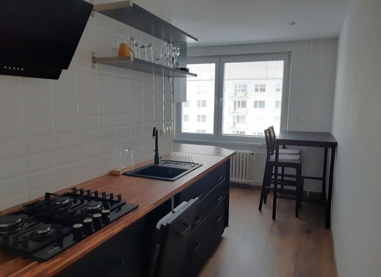 Két szobás lakás konyhája fa mintázatú padlóval és bárasztallal.
