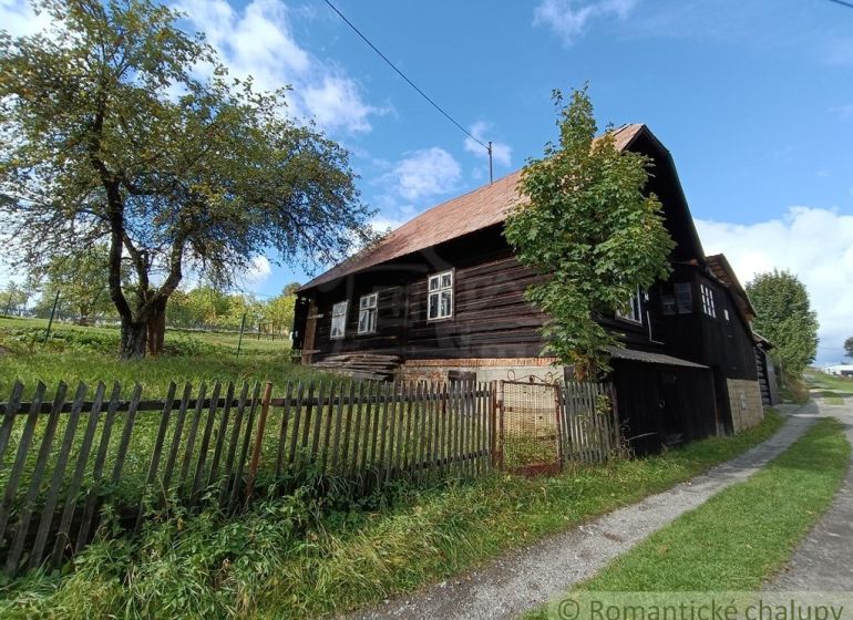 Fából készült ház Staškovban, amelyet fű és fák vesznek körül a kerítés mögött.