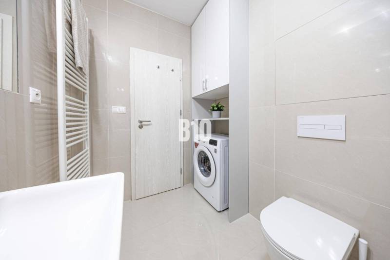 Kúpeľňa s WC, umývadlom, práčkou, bielymi skrinkami vhodná pre 2-izbový byt.