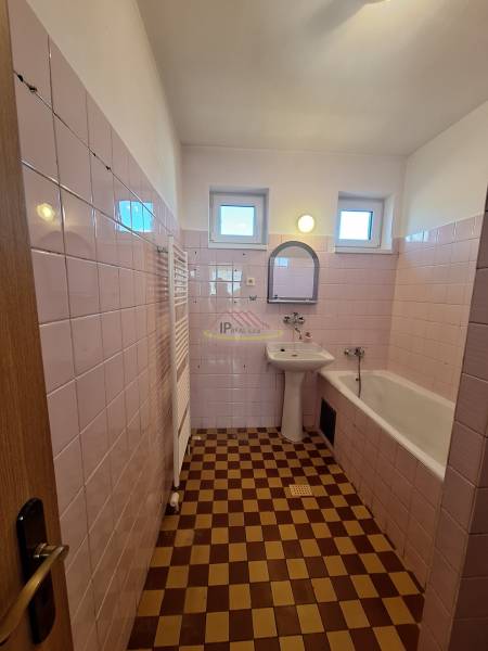 Kúpeľňa s ružovými stenami a dlaždicami, bielym umývadlom, vaňou a oknami na ulici Podhájska.