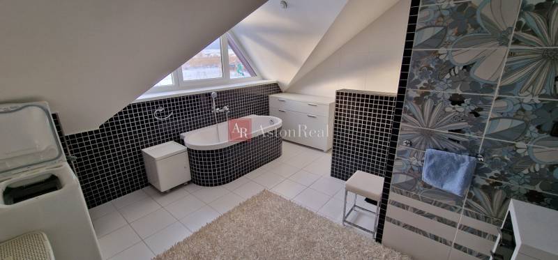 Kúpeľňa v rekreačnom apartmáne so šikmým stropom, čiernobielou dlažbou a vaňou.