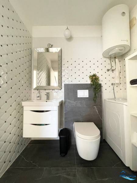 Fürdőszoba a nyaraló apartmanban tárolóhellyel, tükörrel és mosógéppel.