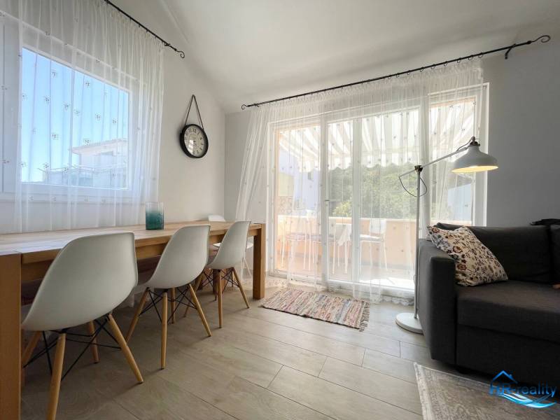 A nyaraló apartman világos nappalit kínál étkezőasztallal és kényelmes kanapéval.
