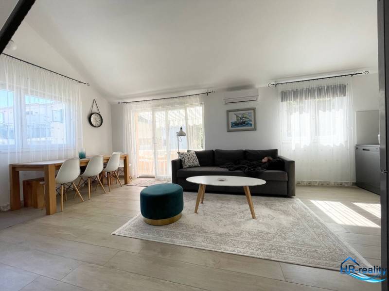Tágas nappali rekreációs apartman kényelmes ülőgarnitúrával és étkezőasztallal.