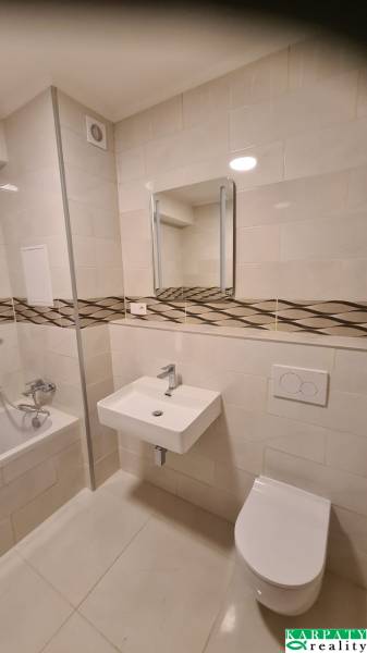 Fürdőszoba egy egyszobás lakásban káddal, mosdóval és WC-vel, csempék dekoratív szalaggal.
