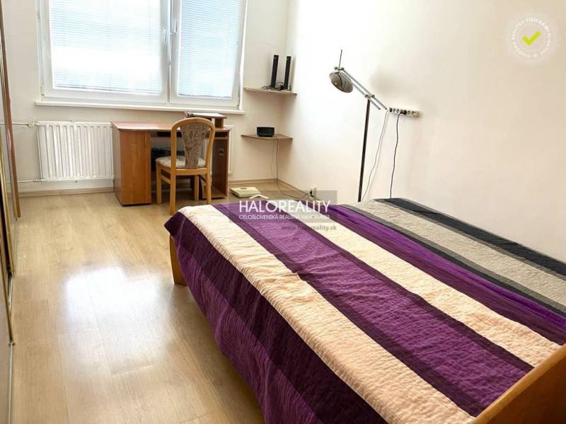 Hálószoba egy háromszobás lakásban ággyal, íróasztallal és fa padlóval.