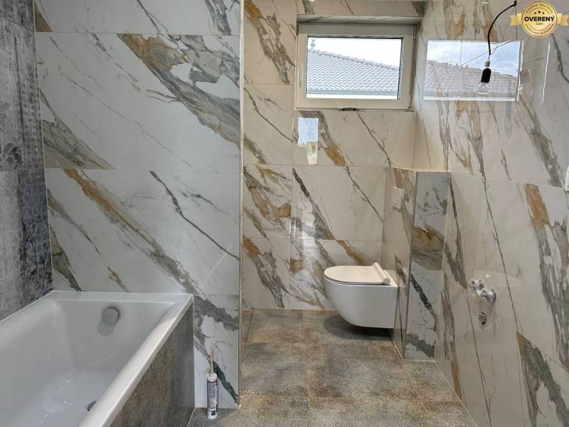 Családi ház fürdőszobája márványmintával burkolva, káddal és WC-vel.