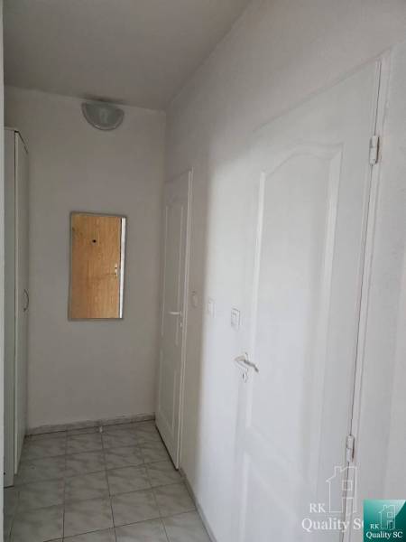 Folyosó tükörrel egy kétszobás lakásban, fehér falak és ajtók, csempe a padlón.
