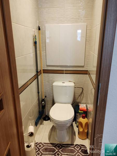 WC a háromszobás lakásban tisztítószerek tárolására szolgáló hellyel.