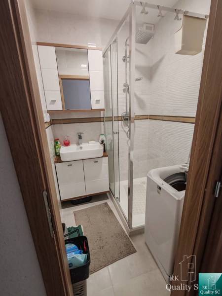 Fürdőszoba egy háromszobás lakásban zuhanyzóval, mosdóval és mosógéppel.