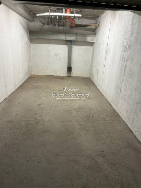 Zárt garázstér betonpadlóval és fehér falakkal, 19-es szám, csövek a mennyezeten.