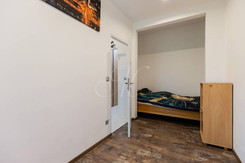 Kis hálószoba ággyal és fa padlóval egy 4 szobás lakásban.