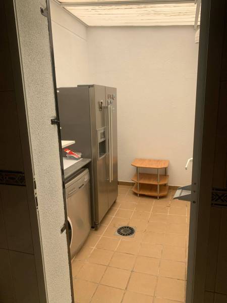 Mosókonyha családi házban hűtőszekrénnyel, mosógéppel és kis asztallal a csempézett padlón.