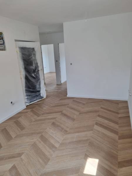 Négy szobás lakás részben befejezett területe, ahol fa padló van lerakva.