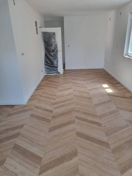 Négy szobás lakás belső tere új fa padlóval és ablakból érkező világítással.
