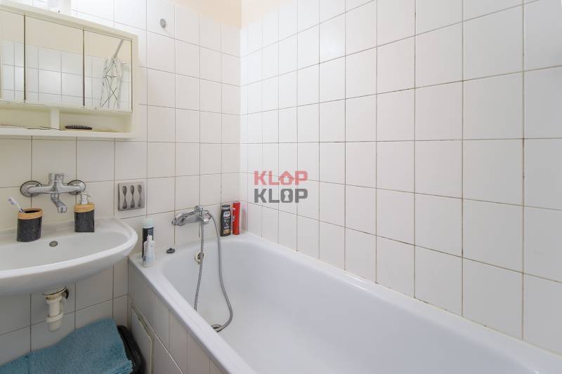 Fürdőszoba káddal, mosdóval és fehér csempékkel egy egyszobás lakásban.