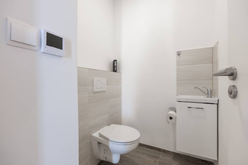 WC és mosdó egy családi házban fehér falakkal és világos csempékkel.