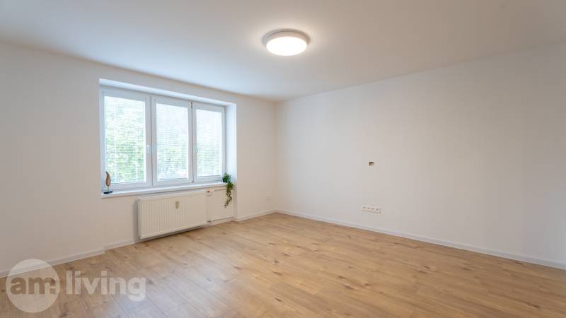 Tágas szoba nagy ablakkal és fa padlóval egy egyszobás lakásban.