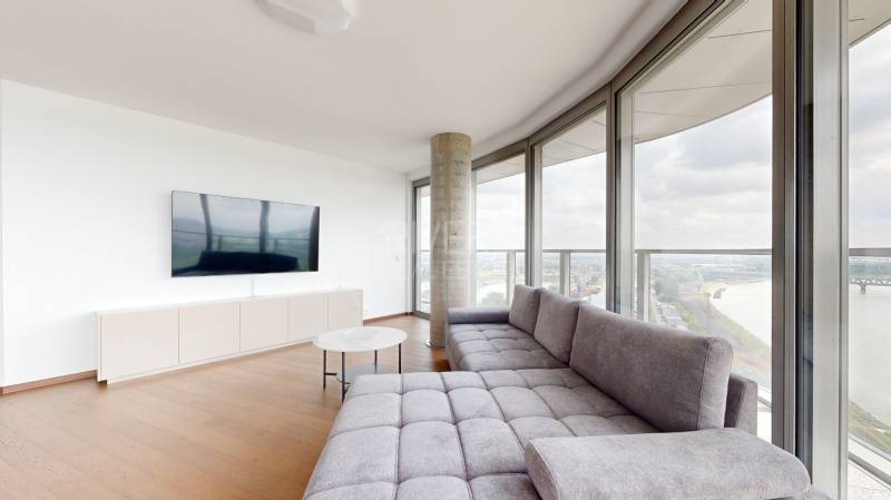 Nappali egy négyszobás lakásban kanapéval, televízióval és panorámás kilátással a folyóra.